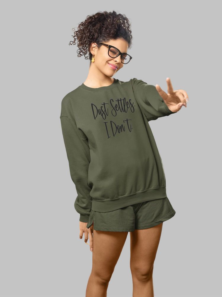 mage of an army green crewneck sweatshirt with the bold statement 'Dust Settles, I Don't' printed on the front. The text is in a distinctive black puff font, giving it a raised, tactile appearance. The phrase stands out against the military-inspired green background, symbolizing resilience and a dynamic spirit.