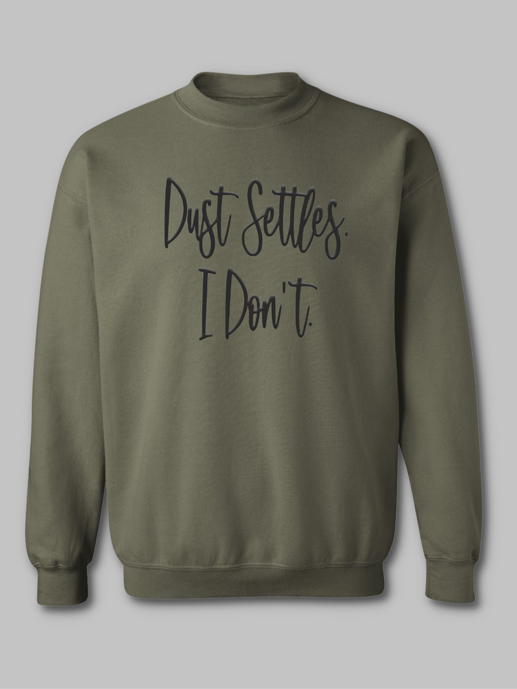 mage of an army green crewneck sweatshirt with the bold statement 'Dust Settles, I Don't' printed on the front. The text is in a distinctive black puff font, giving it a raised, tactile appearance. The phrase stands out against the military-inspired green background, symbolizing resilience and a dynamic spirit.